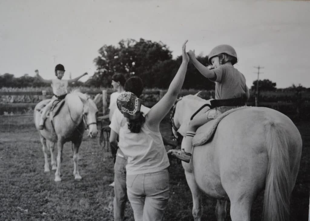 A young Sara Foszcz gives a high five to a rider during an adaptive riding lesson.
