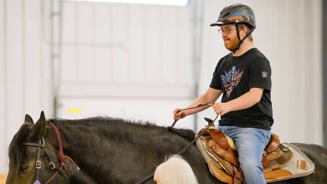 A Main Stay rider smiling while riding their horse during an adaptive riding lesson.