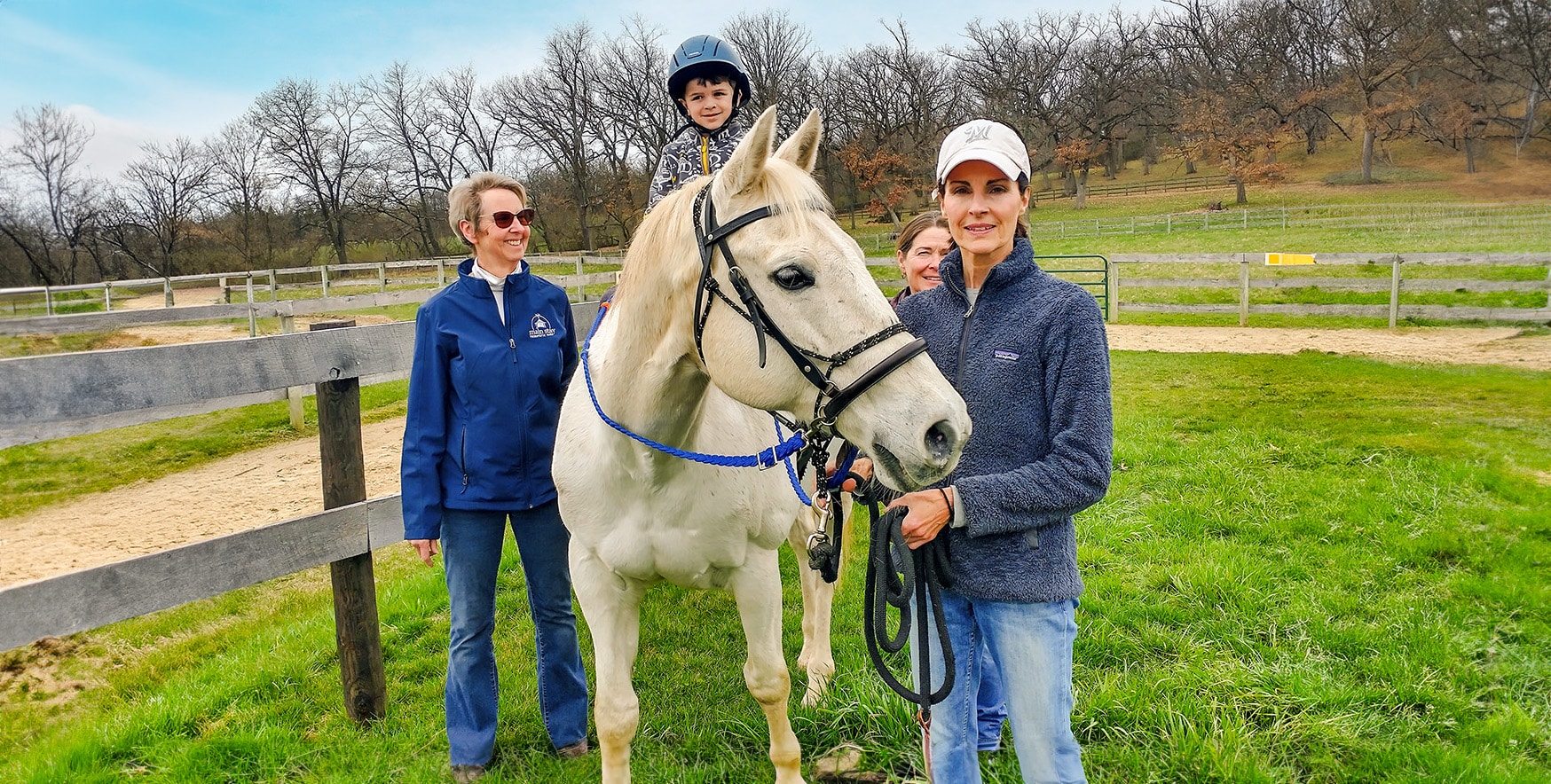 Main Stay volunteers smile while standing next to a white horse and its rider, during an adaptive riding session