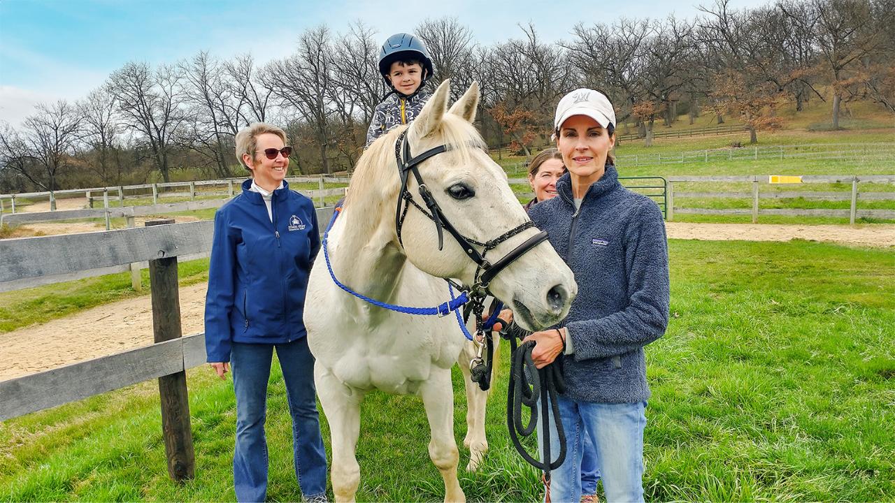 Main Stay volunteers smile while standing next to a white horse and its rider, during an adaptive riding session