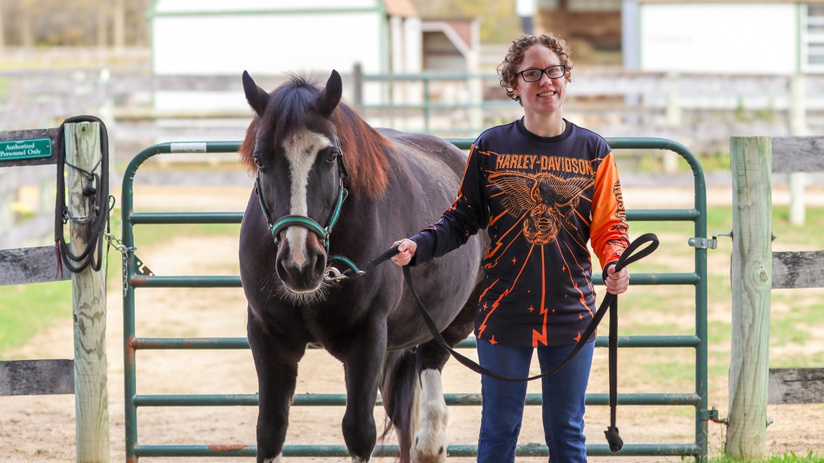 A participant smiles while holding the reins of an adaptive riding horse at Main Stay Farm