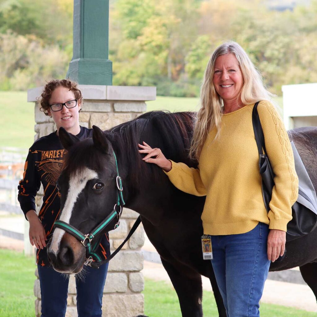 Two participants smile while next to an adaptive riding horse at Main Stay Farm