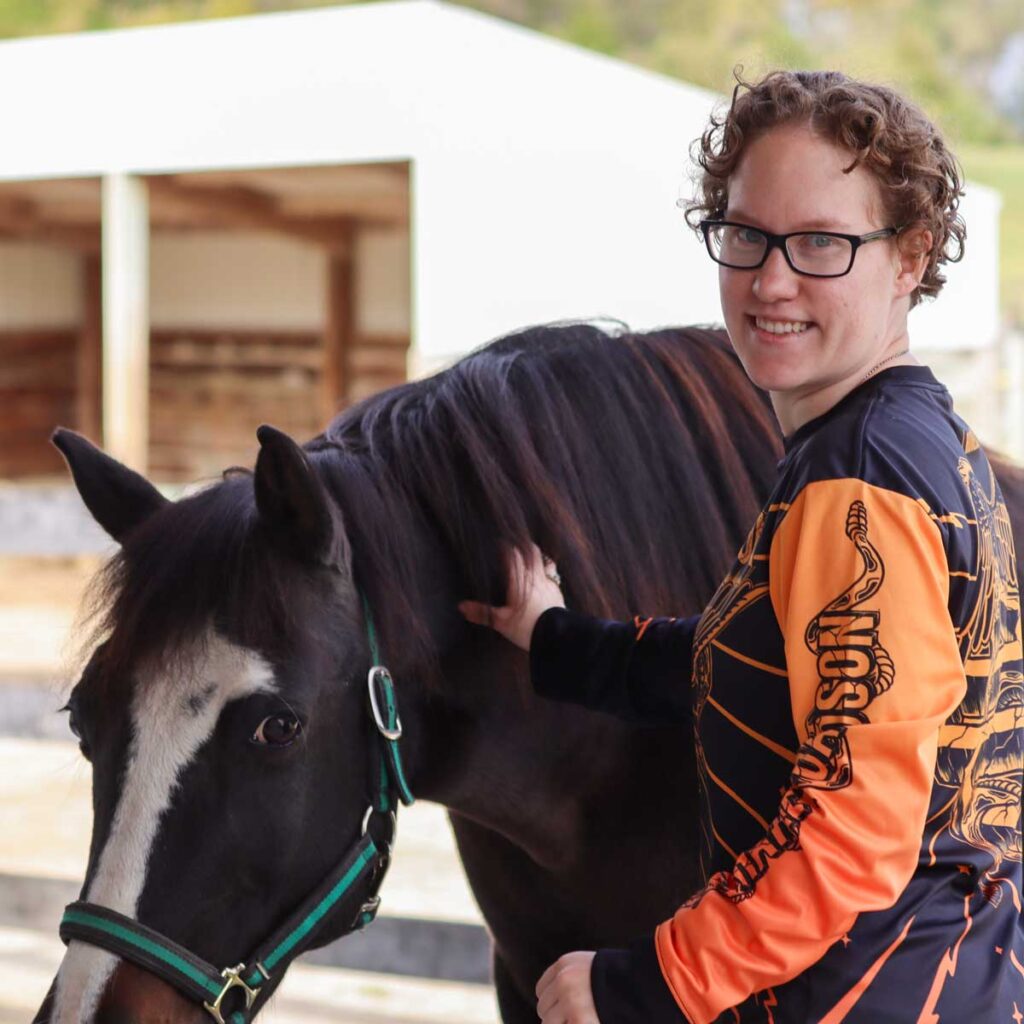 A participant smiles while next to an adaptive riding horse at Main Stay Farm