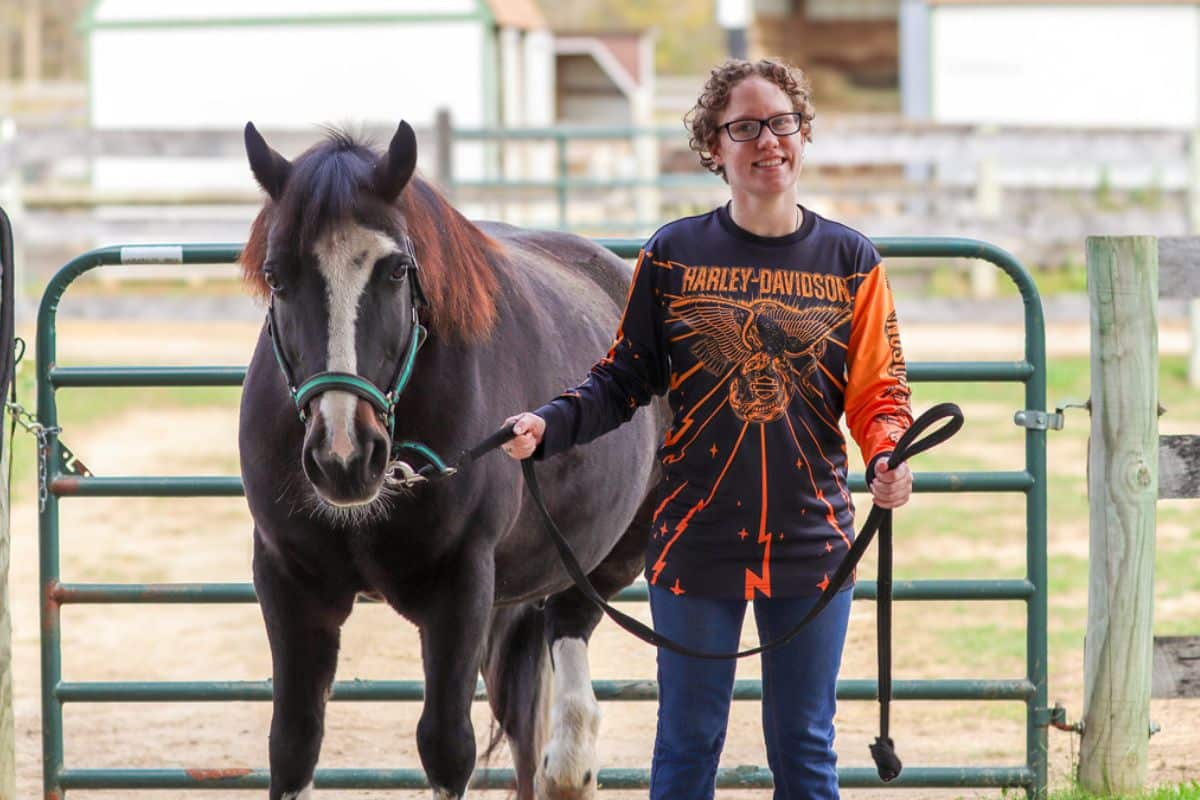 A participant smiles while holding the reins of an adaptive riding horse at Main Stay Farm