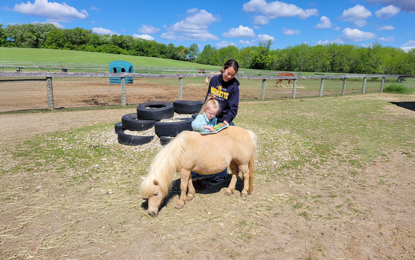 An older student helps a young student read a book that is seated on a miniature horse at Main Stay Farm, showcasing Books in the Barnyard’s animal-assisted approach to literacy.