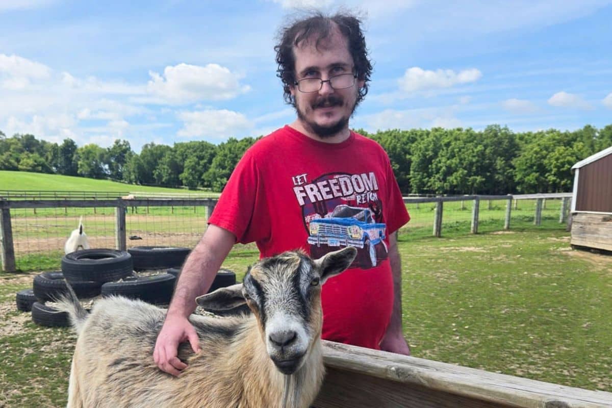 A Main Stay participant smiles next to a goat during an Equine and Animal Assisted Learning session.